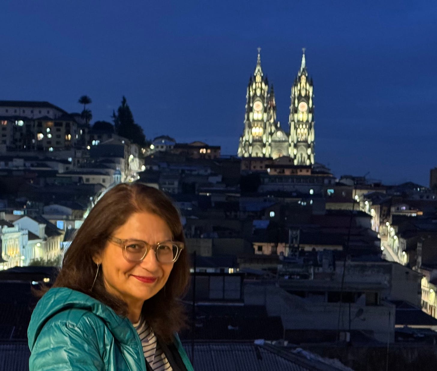 Foto de la autora de noche en Quito. Al fondo se ve iluminada la basílica del Voto Nacional.  Foto archivo propio.