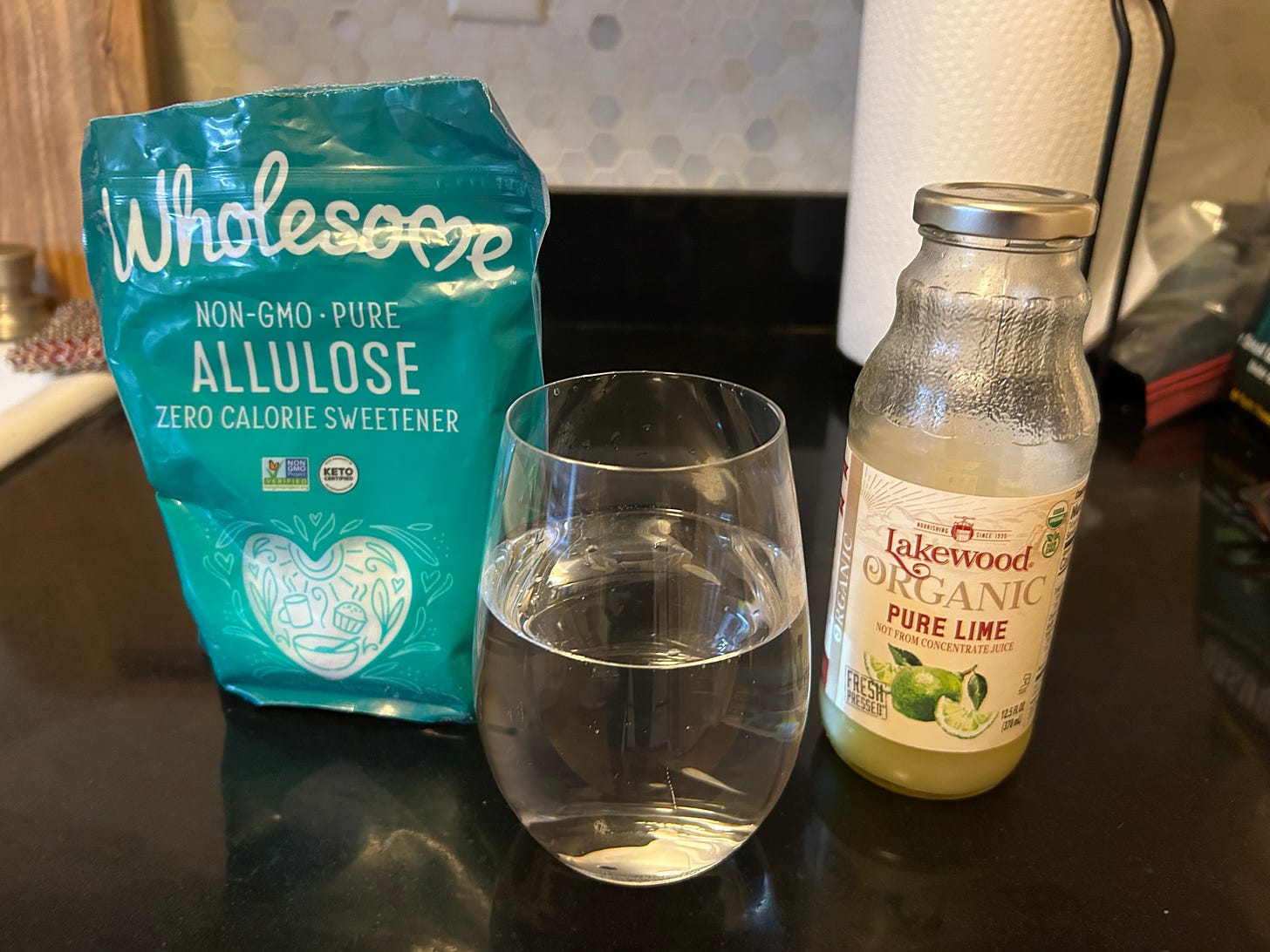 a bag of allulose, a glass of water, and a bottle of lime juice