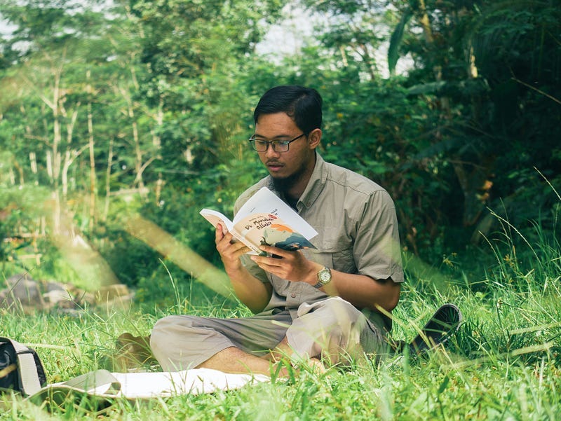 Man reading a book sitting on grass Man reading a book sitting on grass