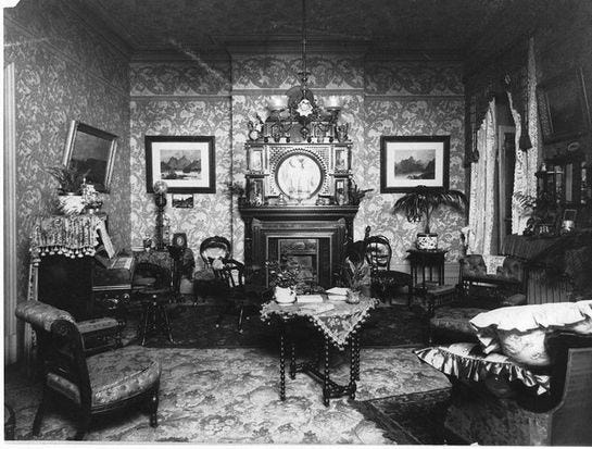 This may contain: an old black and white photo of a living room with couches, chairs, fireplace and pictures on the wall