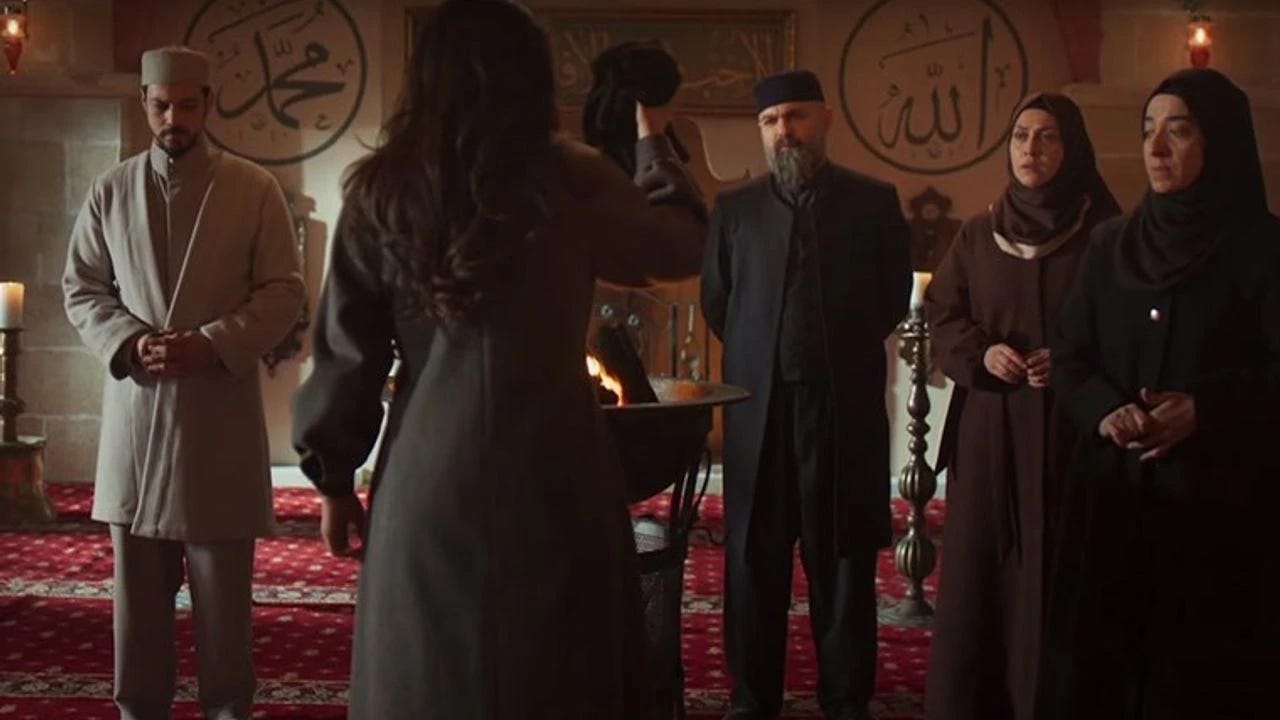 Kadın karakter, dini sembollerle süslenmiş bir mekanda elinde bir nesne tutarak karşısındaki grup ile yüzleşiyor. Arka planda İslam yazıları ve dekoratif objeler yer alıyor.