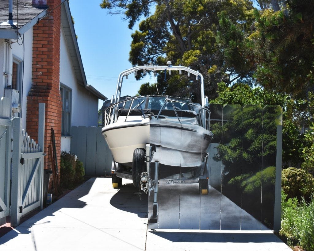A photograph showing a boat in a driveway behind a fence with a boat painted on it