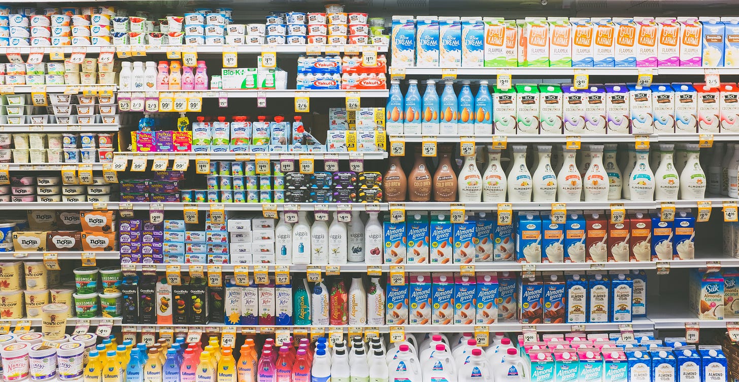 A fridge aisle of a supermarket, containing a variety of different dairy and dairy-alternative products