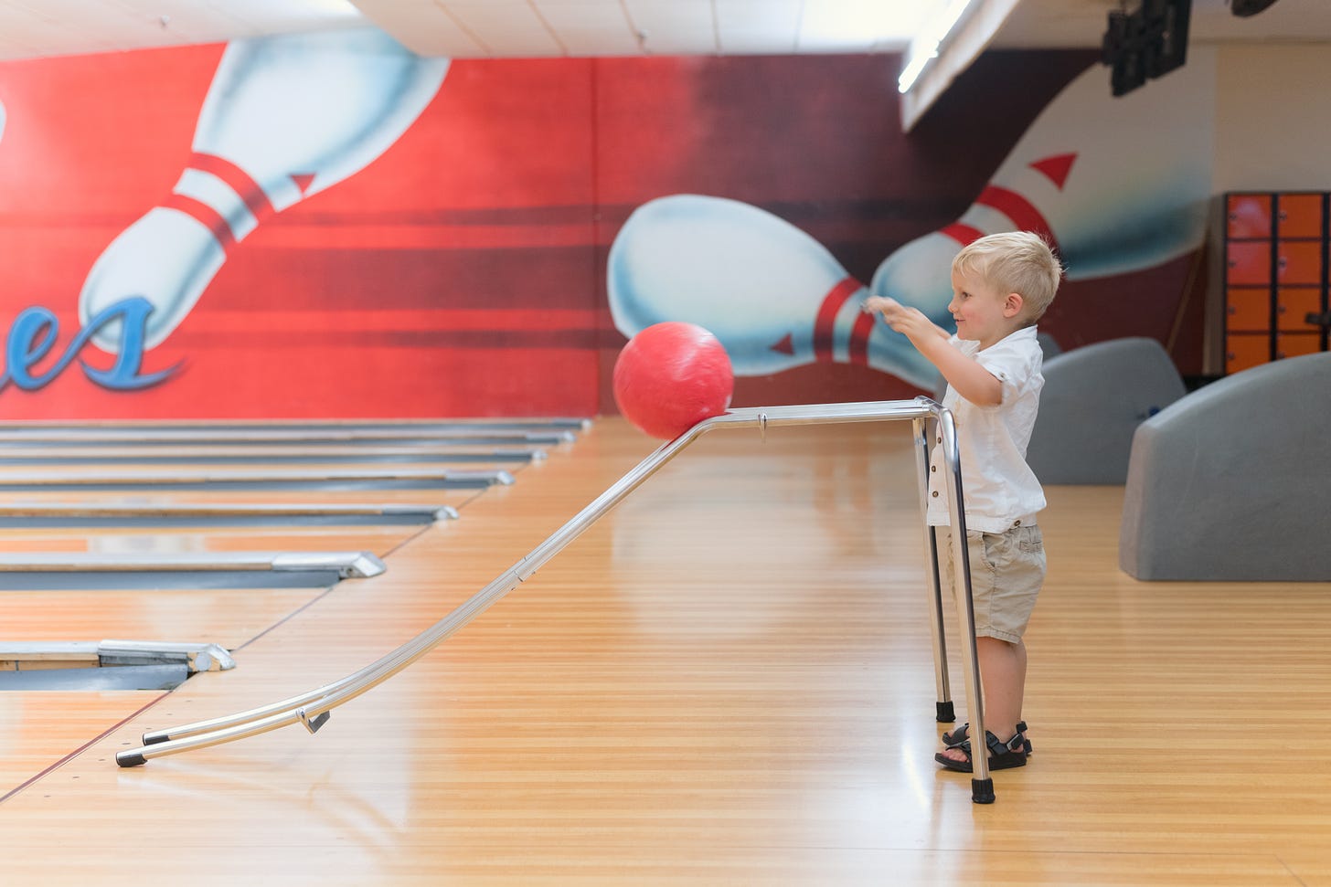 Profile picture of a young boy at a bowling alley. The boy is using a disability-aid stand to roll his bowling ball down the bowling lane.
