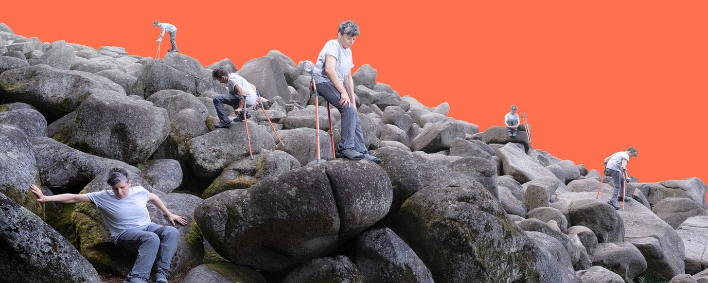 A disabled white artist is in many places at once across a hill of large grey rocks. She uses orange crutches in several places, variously in motion and at rest.