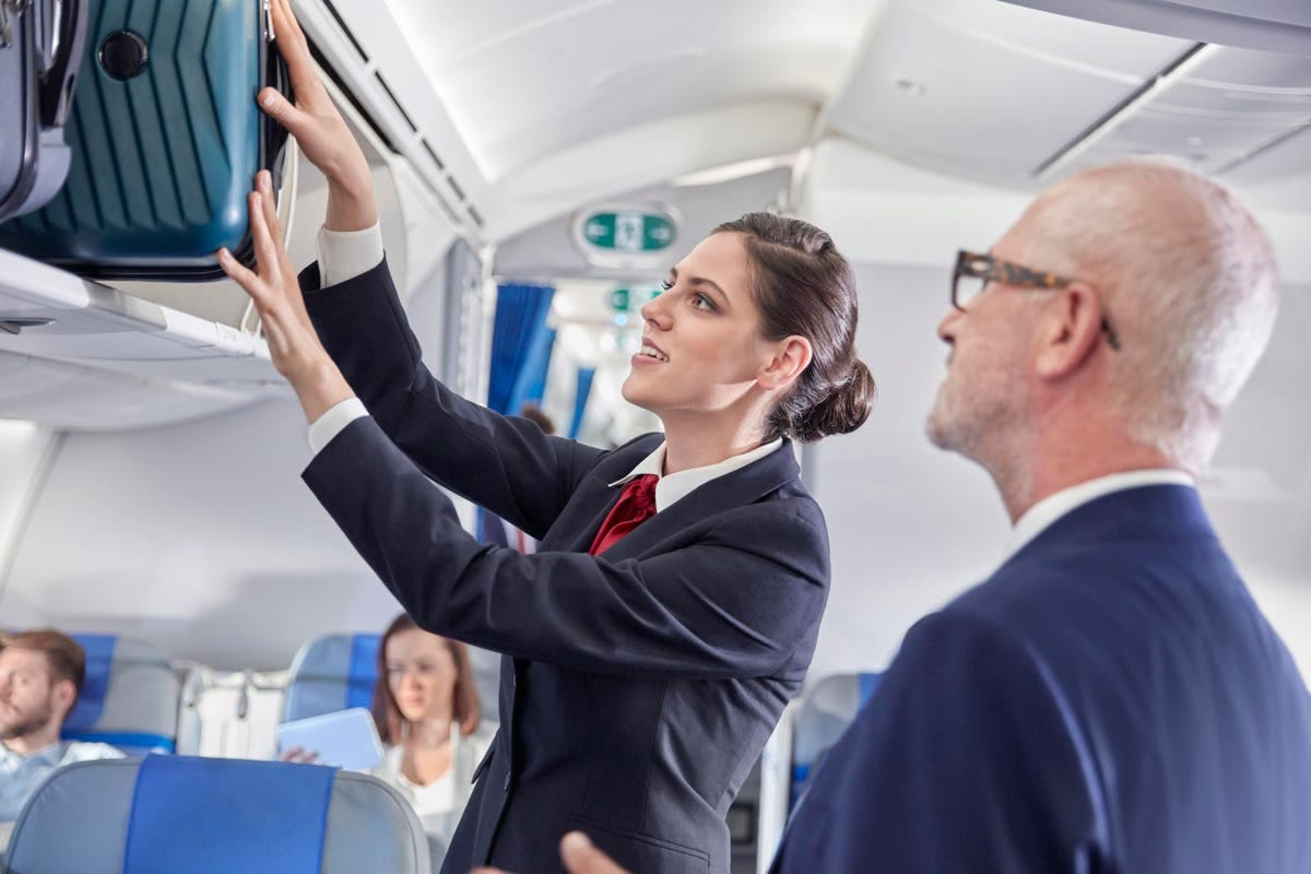 A Delta flight attendant helps with the luggage of a business traveler enroute