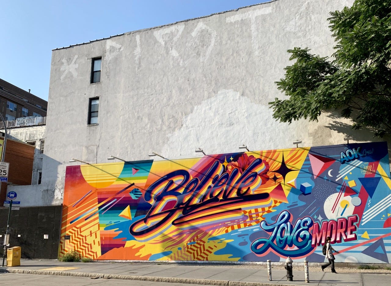 Photo of the side of a building showing a colourful graffiti mural saying "Believe... Love More".