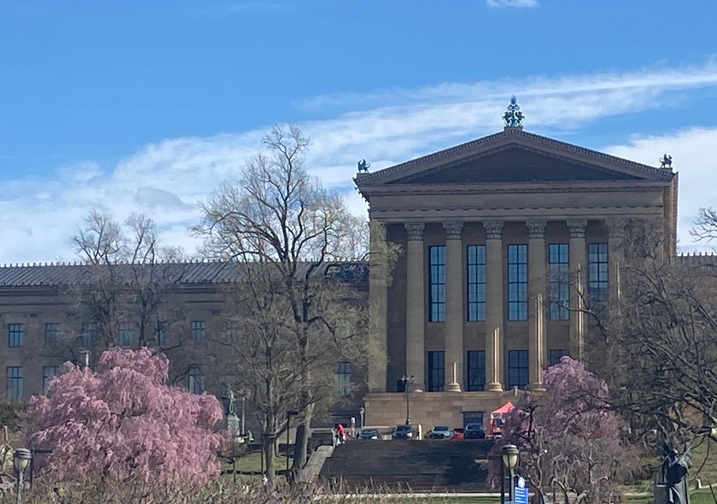The back of the Philadelphia Ar Museum, a building with tall roman columns. In fron tof the museum are two blooming cherry tress.