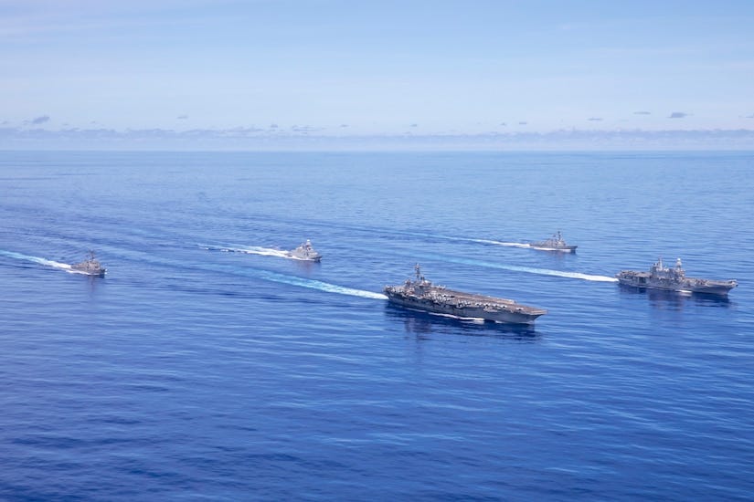 An aerial view of five large naval vessels sailing on the ocean.