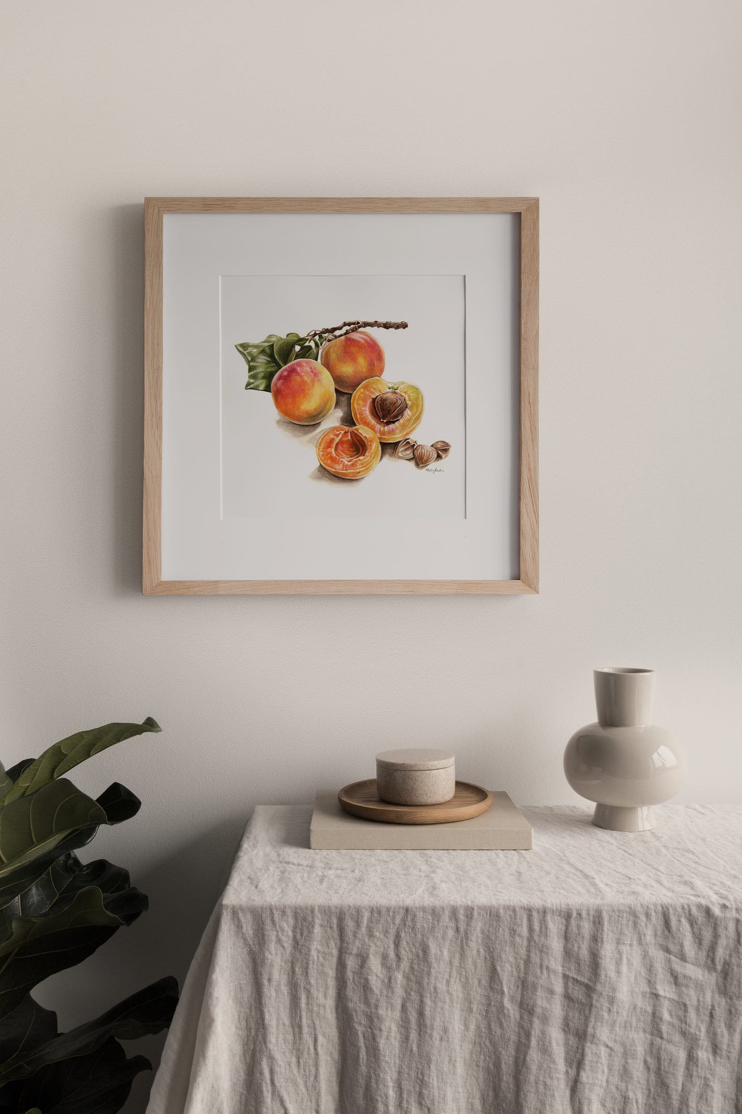 a framed and matted print of bright orange apricots, hanging above a white tablecloth covered table