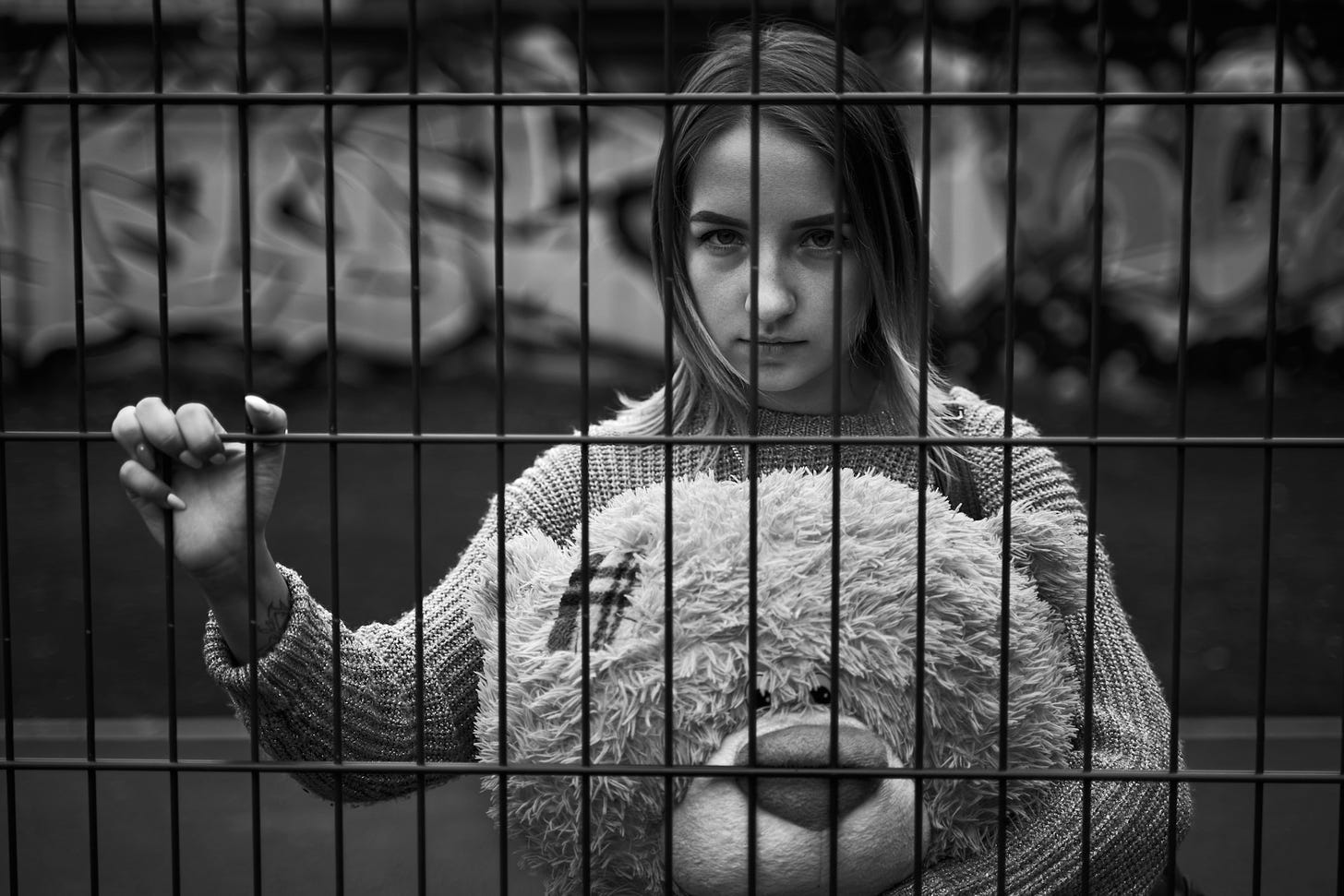 Woman holding toy bear, behind jail bars