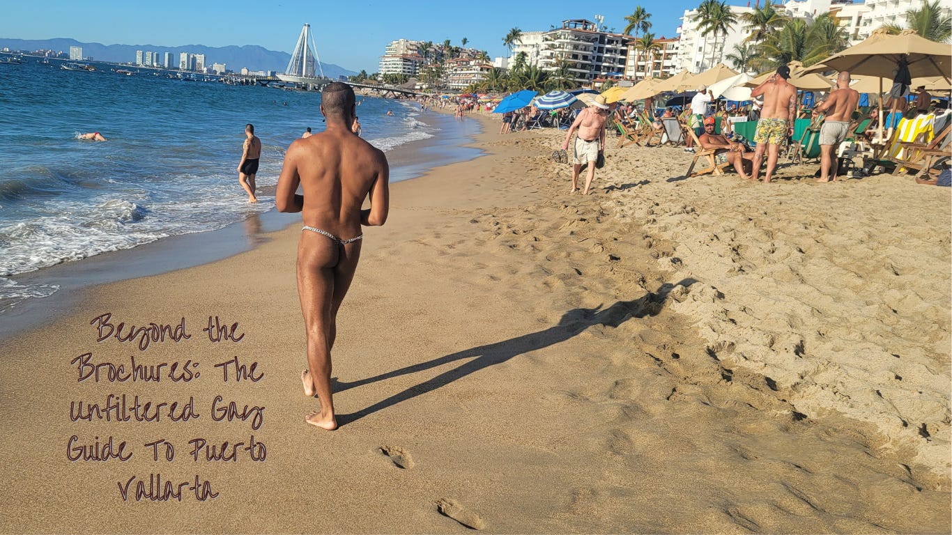 A sunlit beach in Puerto Vallarta with a clear blue sky. Tomik Dash, seen from the back, stands close to the camera, wearing a chain-thong swimsuit, gazing at the sea. The shoreline features people enjoying the water and lounging under umbrellas. In the background, city buildings and a distinctive bridge rise against a backdrop of distant mountains. The sand bears the handwritten title 'Beyond the Brochures: The Unfiltered Gay Guide to Puerto Vallarta'.