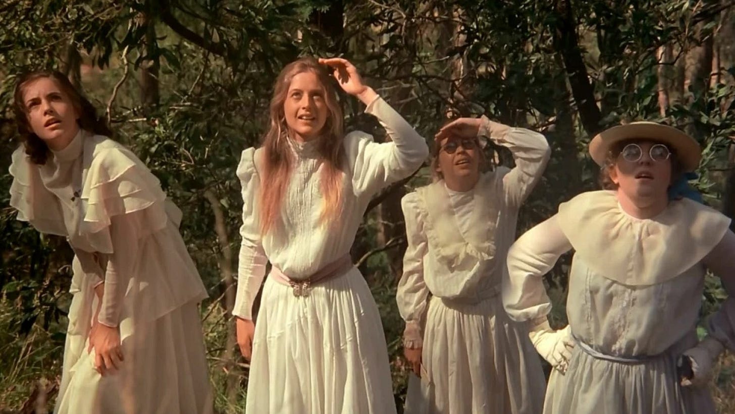 A screenshot from Peter Weir’s 1975 film Picnic at Hanging Rock. In it, four young women in white dresses stare up and out of frame.