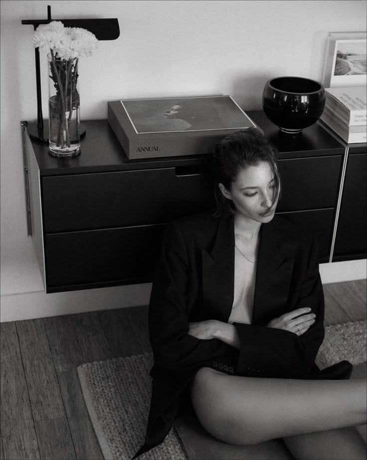 This may contain: a woman sitting on the floor in front of a dresser with her hands folded up