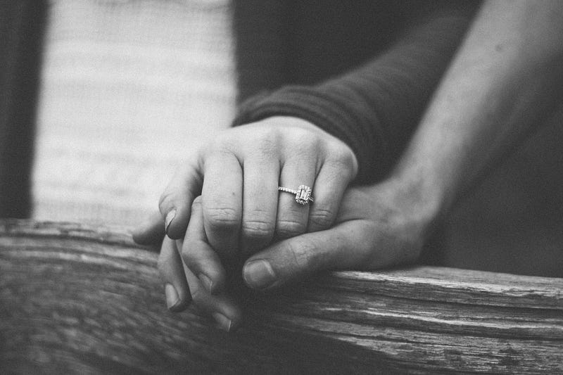 A pair of hands on a railing with a diamond ring on the woman’s hand. A pair of hands on a railing with a diamond ring on the woman’s hand.