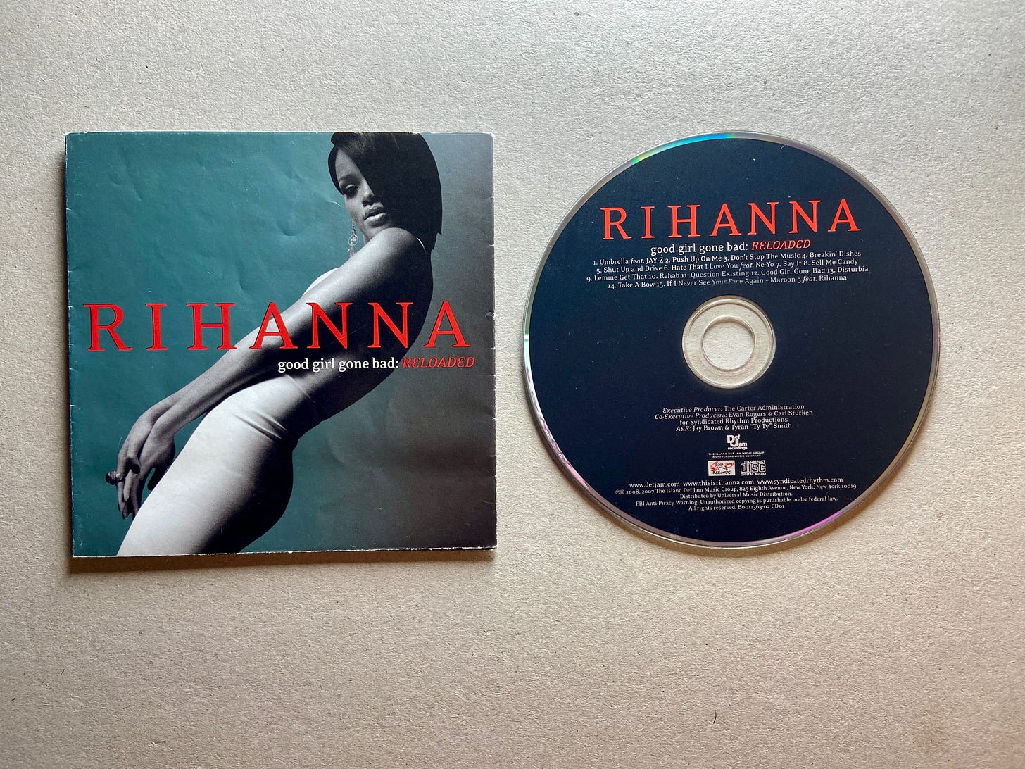 the album insert and CD for Rihanna’s 3rd album, Good Girl Gone Bad: Reloaded (a deluxe album). she wears a white dress while leaning back with red text on the image.