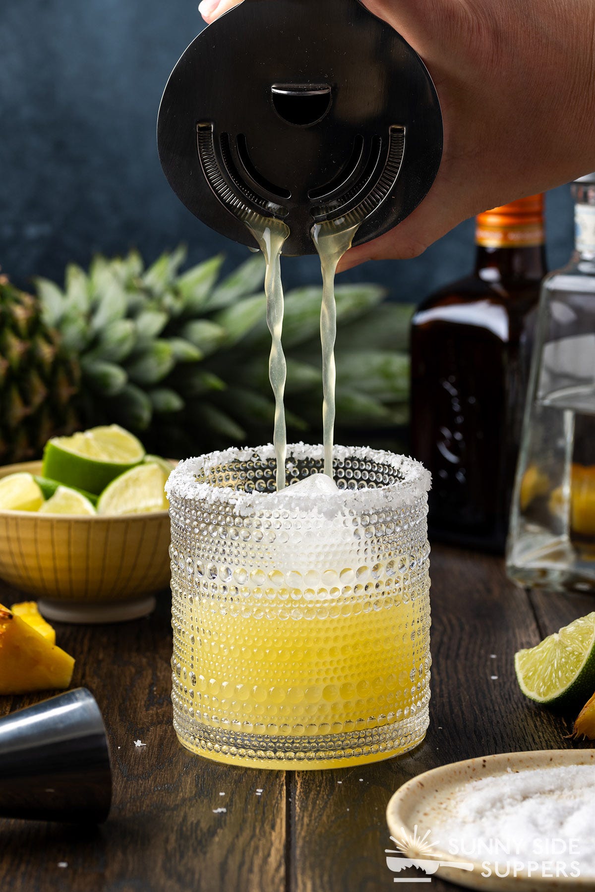 Pouring a pineapple margarita into a cocktail glass with a rim.
