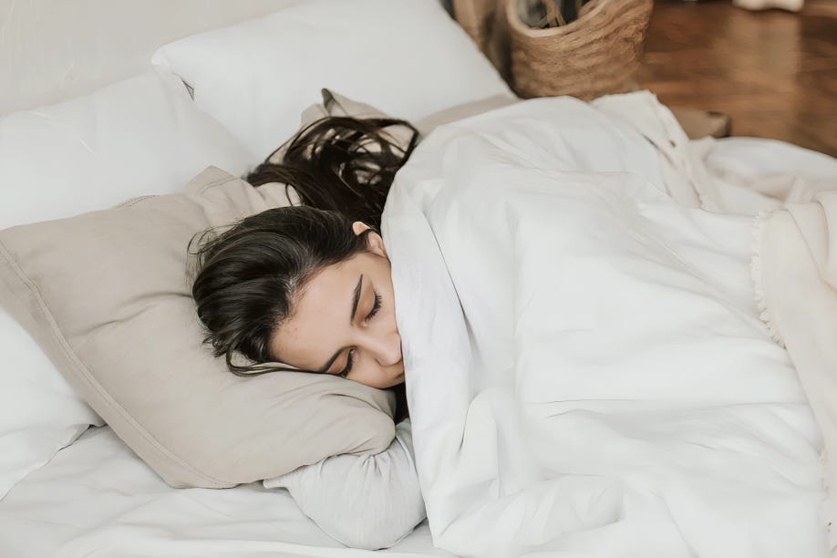 A woman peacefully sleeping in a cozy bed, surrounded by soft blankets and pillows.