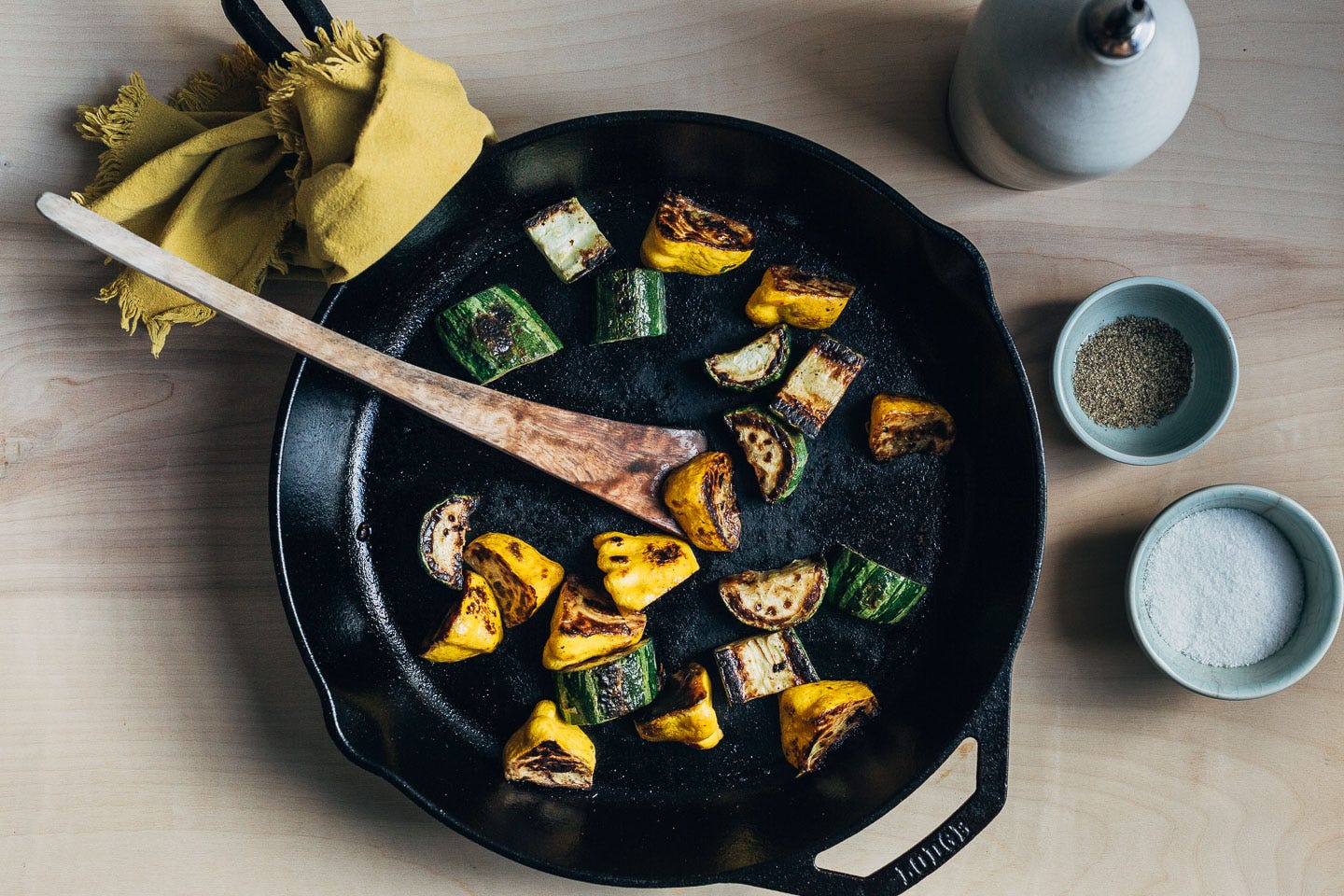 A cast iron skillet with charred squash and a bottle of olive oil salt, and pepper alongside. 