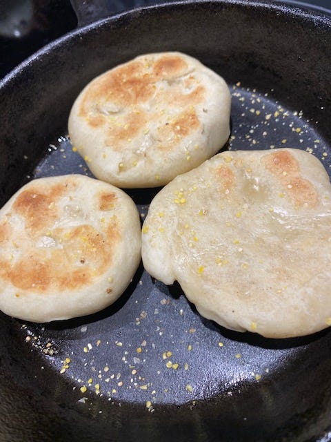 three sourdough English muffins in a cast iron skillet