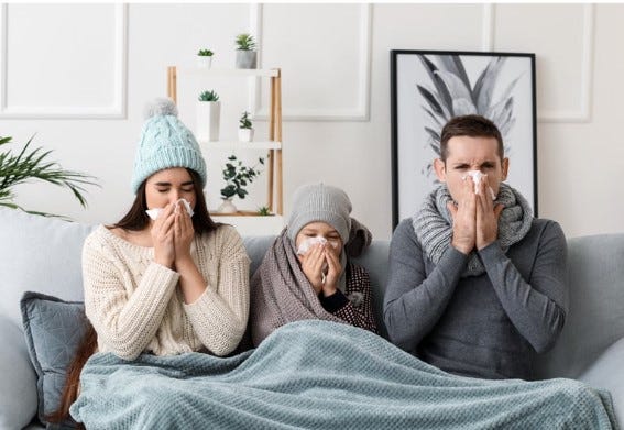 three people sick on a sofa holding tissues to their noses