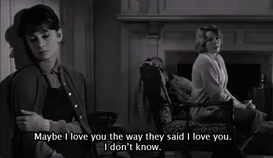 Scena in bianco e nero dal film The Children’s Hour (1961). A sinistra, Karen (Audrey Hepburn) è appoggiata al muro con lo sguardo abbassato, le braccia incrociate sul petto. A destra, Martha (Shirley MacLaine) è seduta su una poltrona davanti al camino, guarda Karen con un’espressione addolorata. In sovrimpressione, i sottotitoli recitano: “Maybe I love you the way they said I love you. I don’t know.” Scena in bianco e nero dal film The Children’s Hour (1961). A sinistra, Karen (Audrey Hepburn) è appoggiata al muro con lo sguardo abbassato, le braccia incrociate sul petto. A destra, Martha (Shirley MacLaine) è seduta su una poltrona davanti al camino, guarda Karen con un’espressione addolorata. In sovrimpressione, i sottotitoli recitano: “Maybe I love you the way they said I love you. I don’t know.”