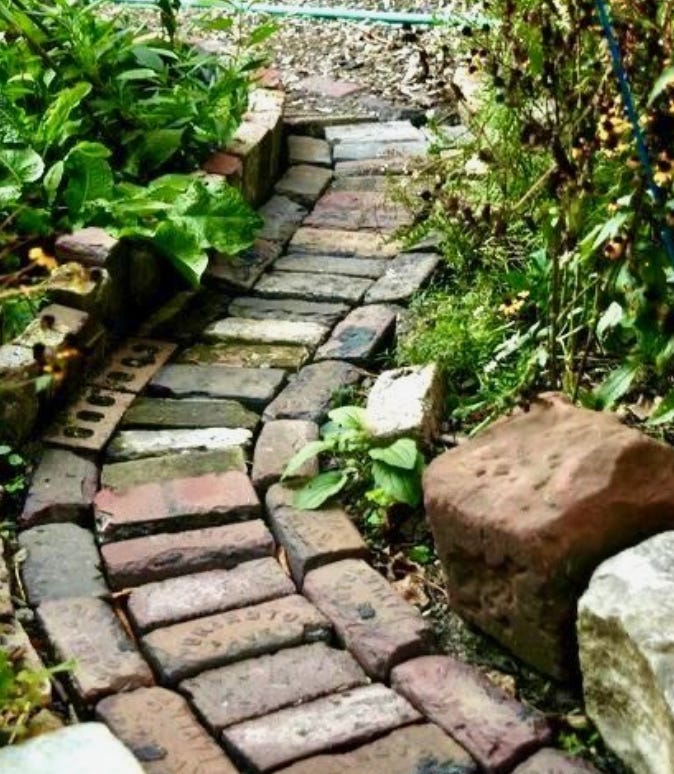 A narrow brick path in a garden flowerbed