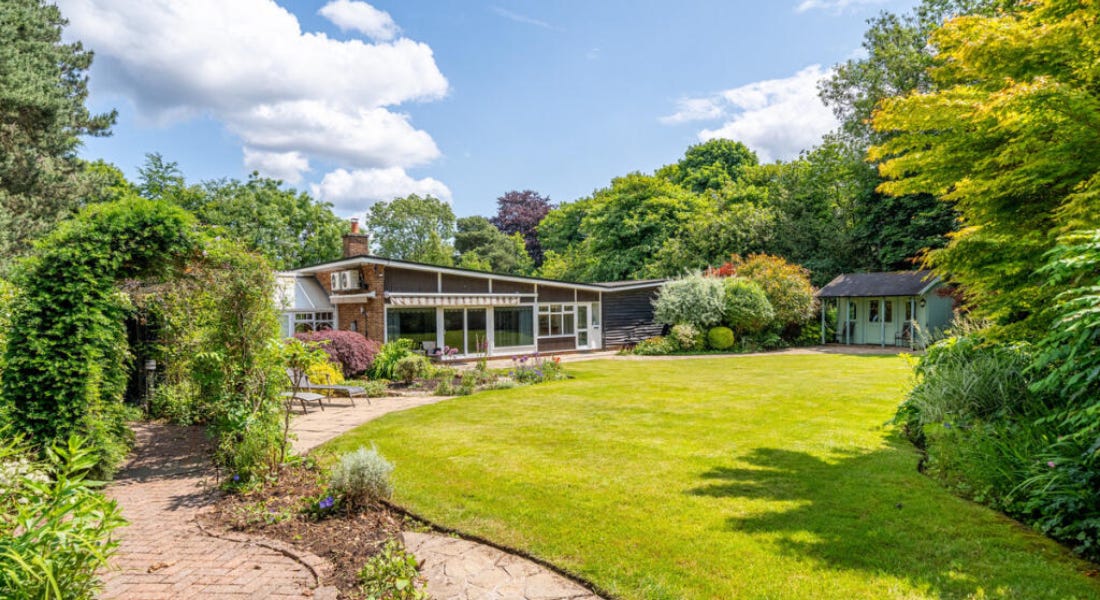 A bungalow with a lawn in front of it, a winding path to the left of it, and trees around it