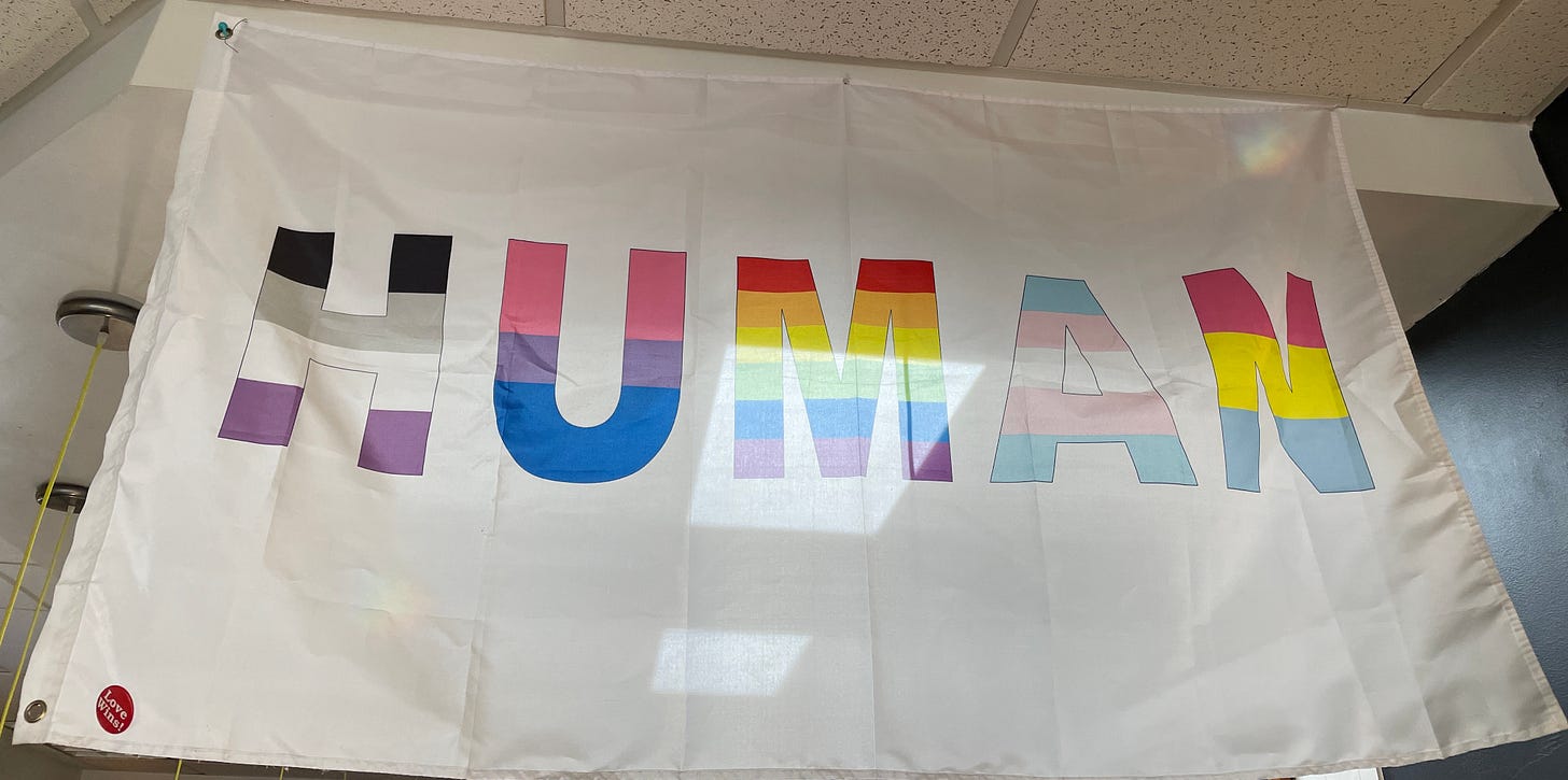 white banner with rainbow all caps letters that say HUMAN