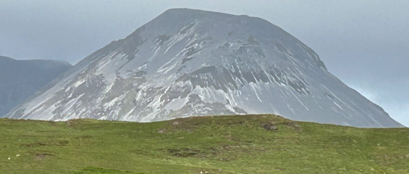 Grey steep sided mountain beyond green slopes