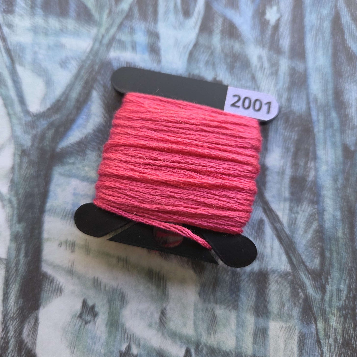 A black embroidery bobbin with a bright pink floss wrapped around it.