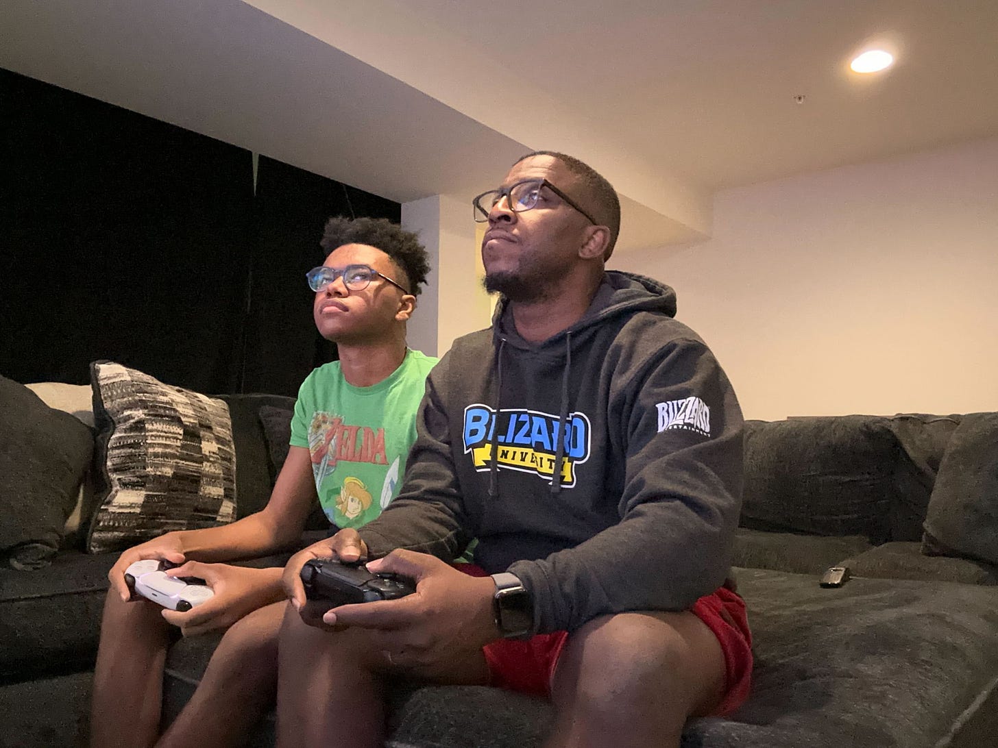 A candid photograph of Max Levasseur and his son Christian playing video games at home.