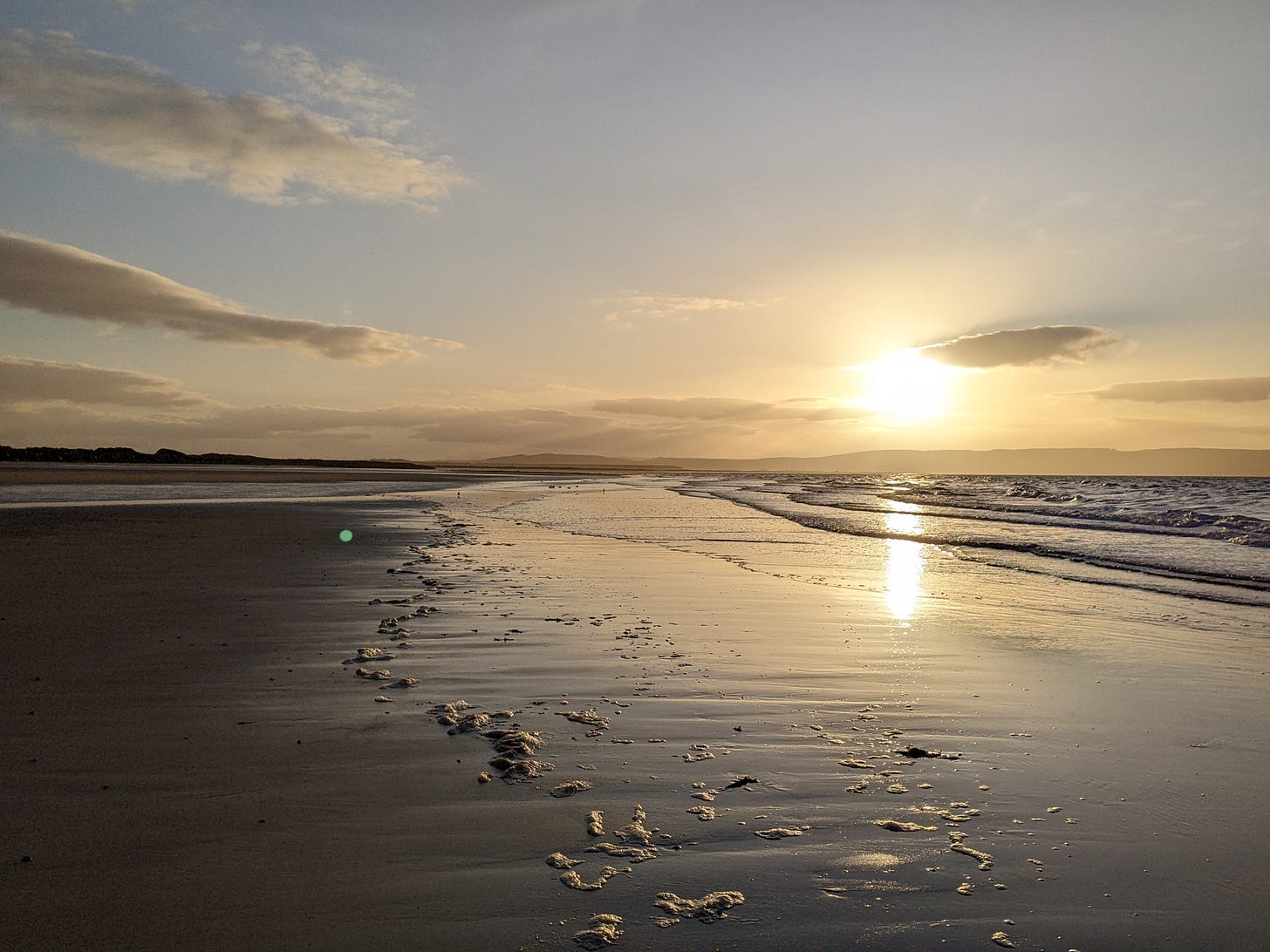 Sandy beach with gentle waves, hills beyond with the setting sun