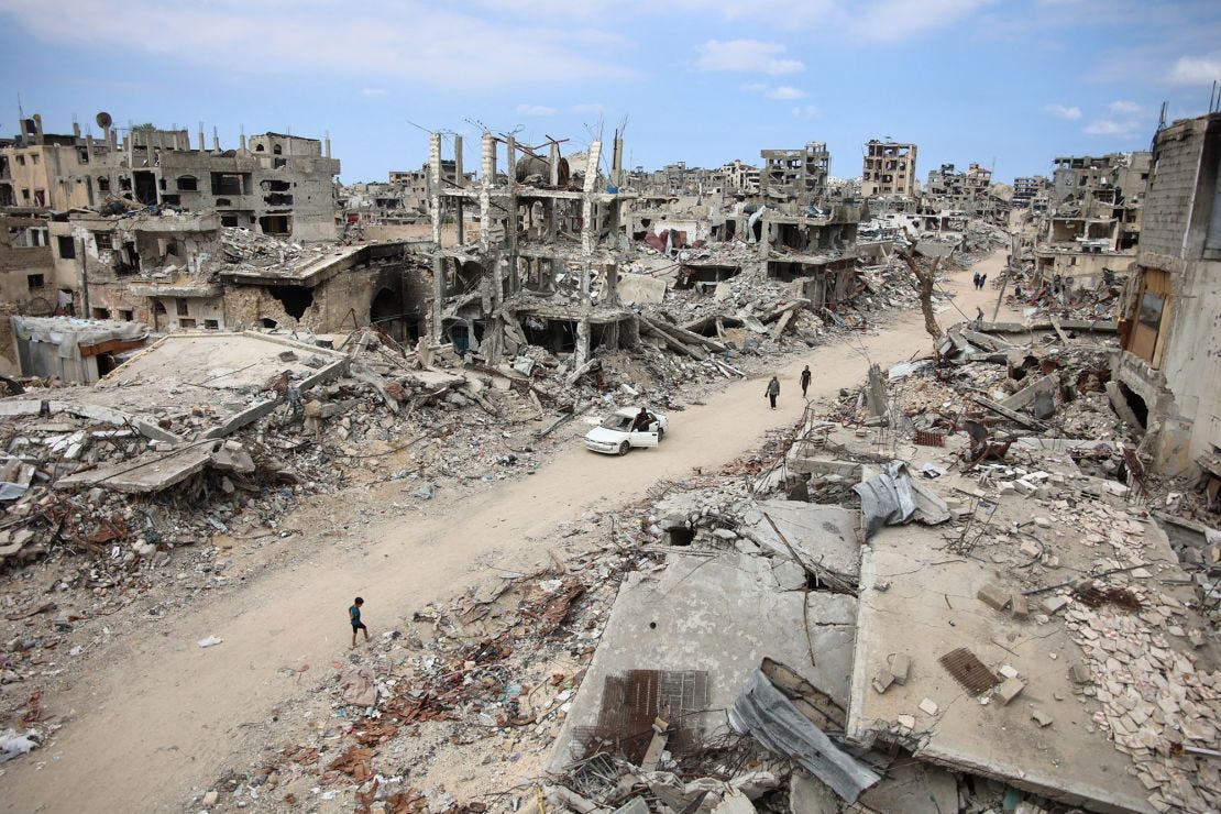 Displaced Palestinians walk on a dirt road lined with building rubble in the Shejaiya neighbourhood of Gaza City on October 7, 2024.