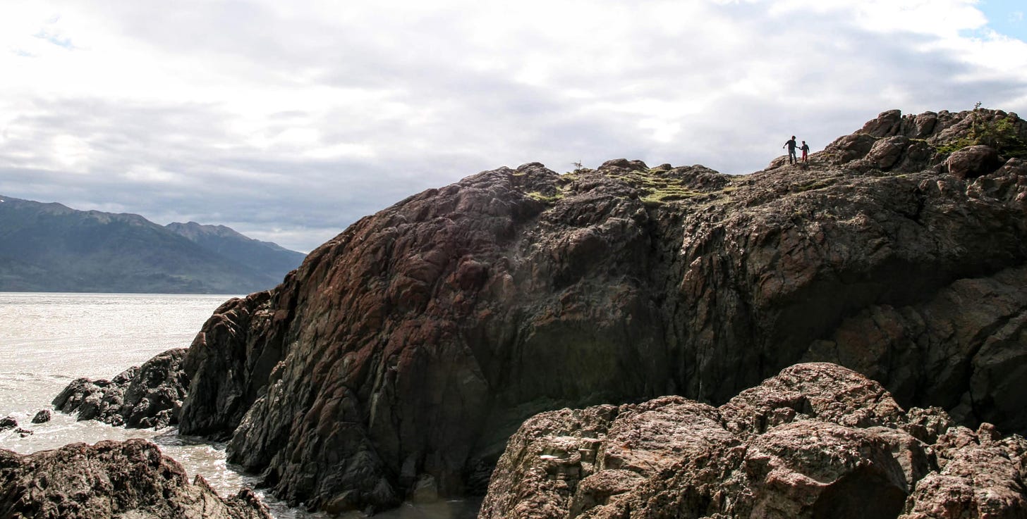 Two people holding hands while walking precariously on a rocky promontory at Turnagain Arm, Alaska.