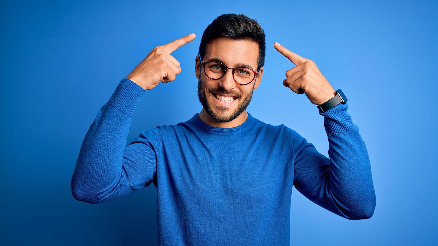 Smiling man in blue sweater and glasses pointing to his head against a blue background.