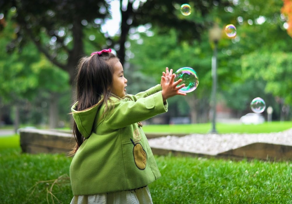 Small asian girl in green jacket catching a large bubble