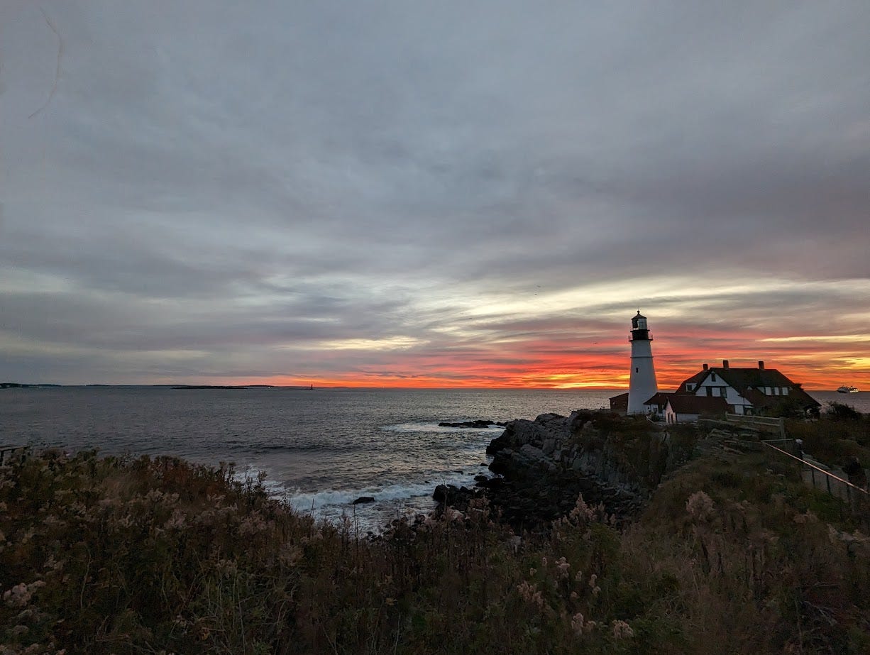 Pink and orange sunrise over the ocean and rocky coastline at the Portland Headlight lighthouse.
