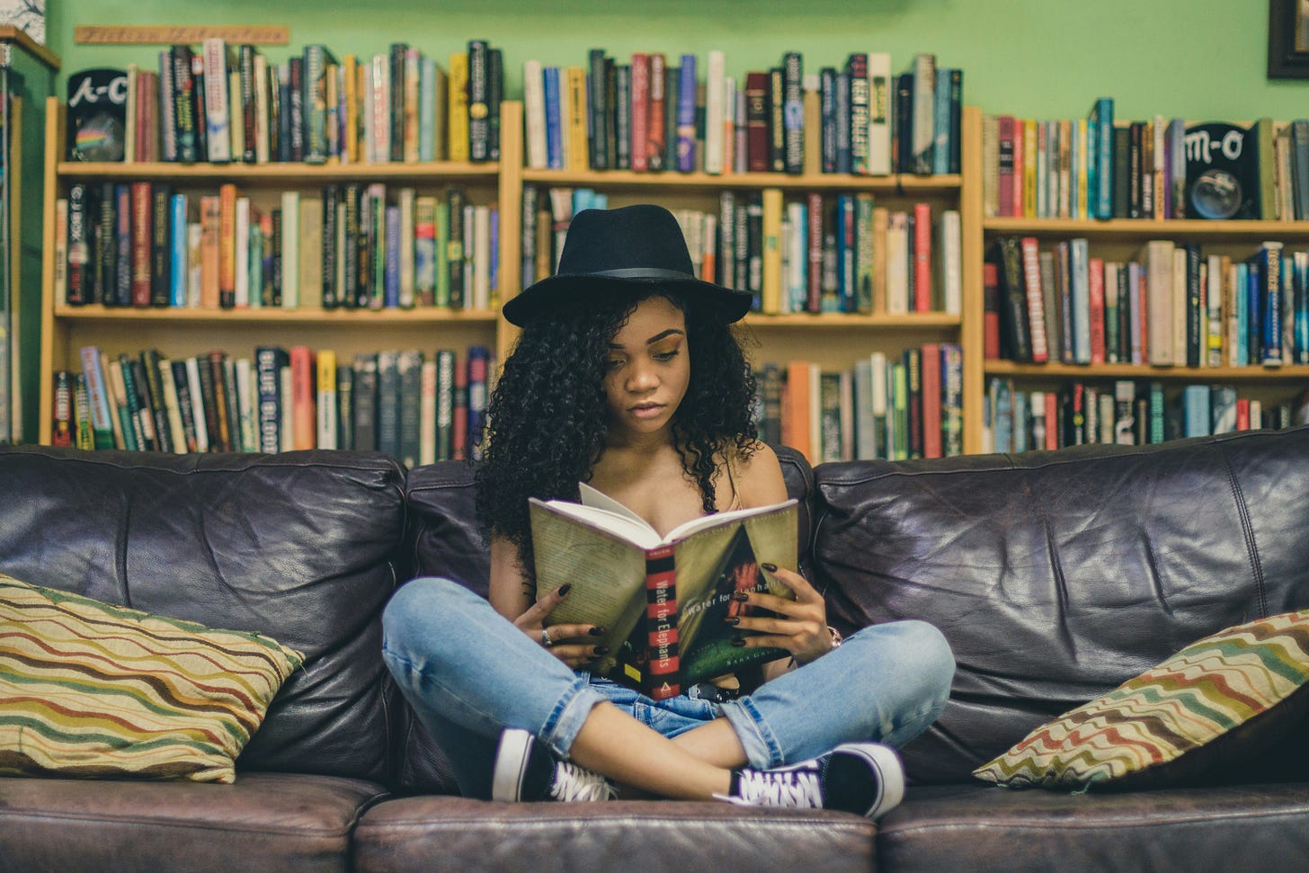 Teen girl sitting and reading on a leather couch in a library