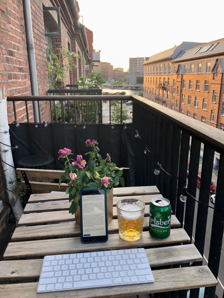 A keyboard, smartphone and glass of beer sit on the table of a balcony overlooking a European street