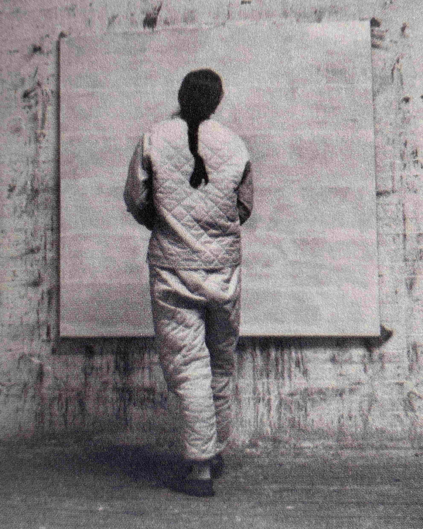 Agnes Martin has her back to us and is working on a big canvas. She's wearing quilted jacket and trousers