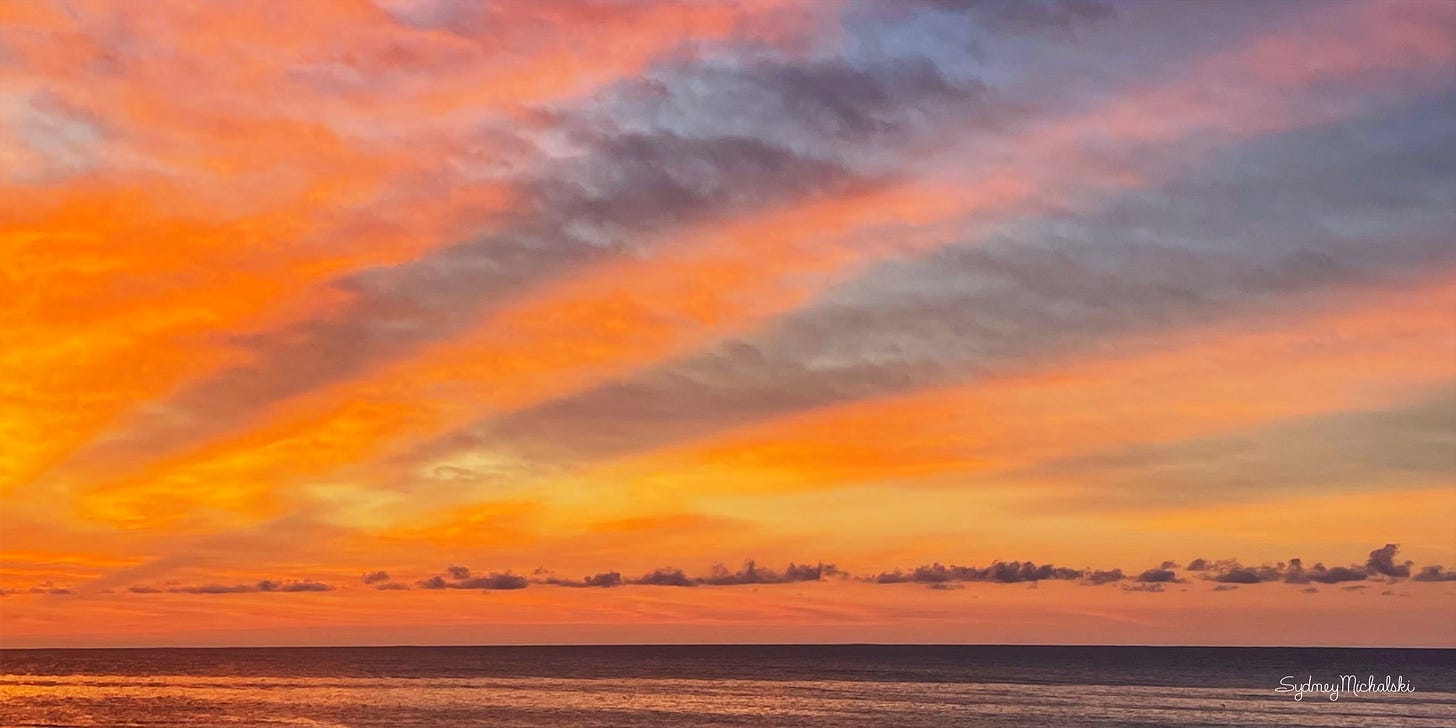 Fiery orange sunrise rays stretch across purple clouds above an ocean horizon.