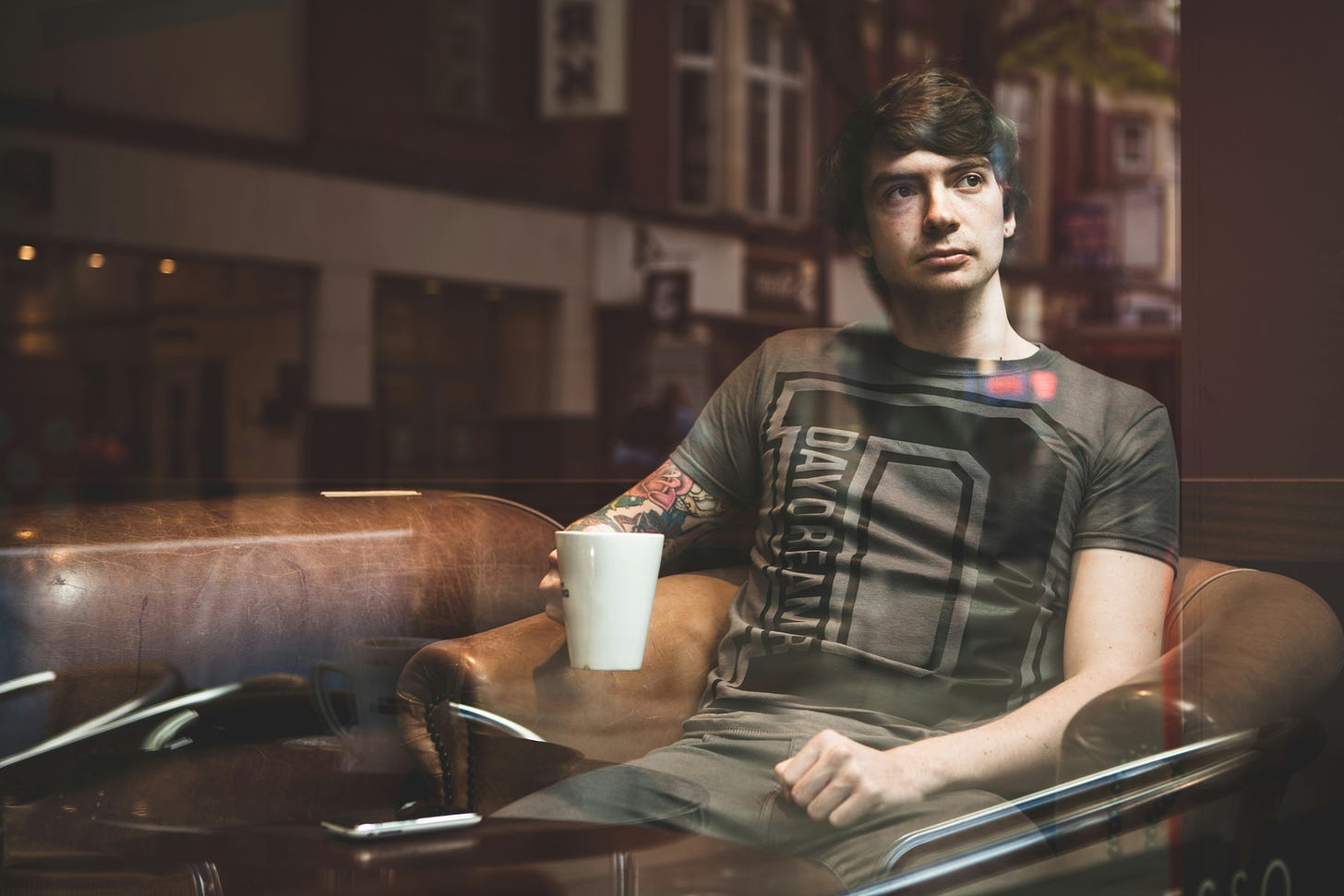 man sitting in brown armchair with coffee cup while looking out window