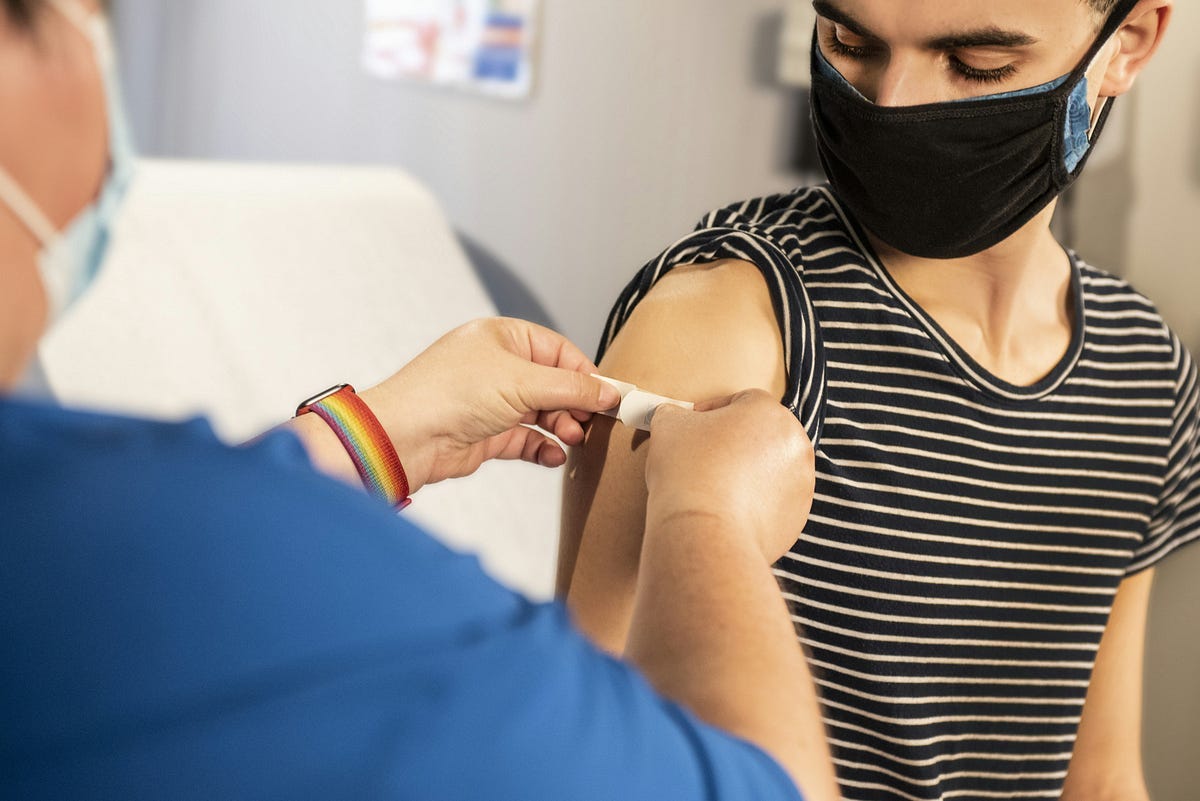 Patient with mask, having plaster to cover injection mark, by doctor