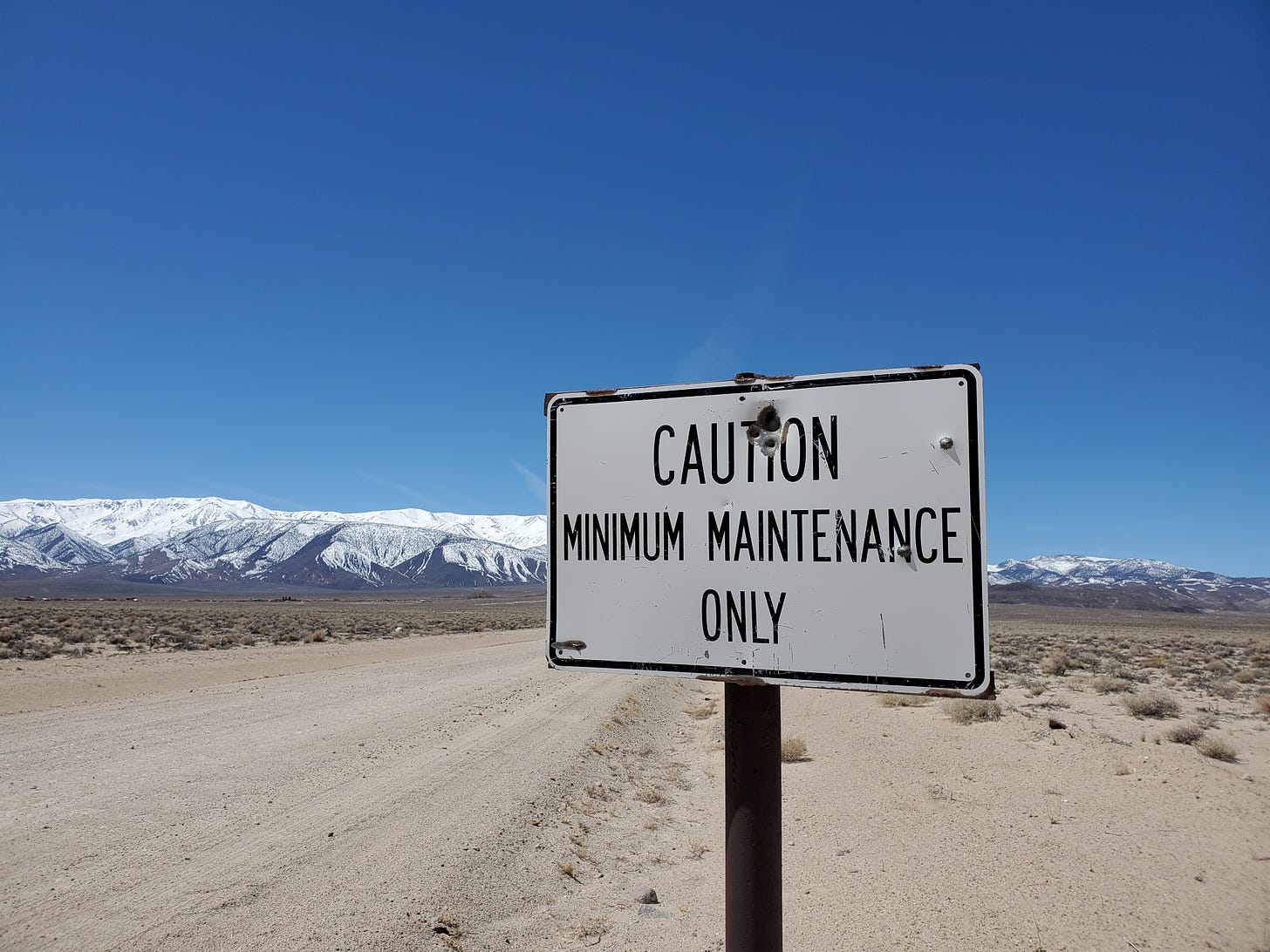 A road sign that says 'Caution Minimum Maintenance Only.' White Mountains in the distance.