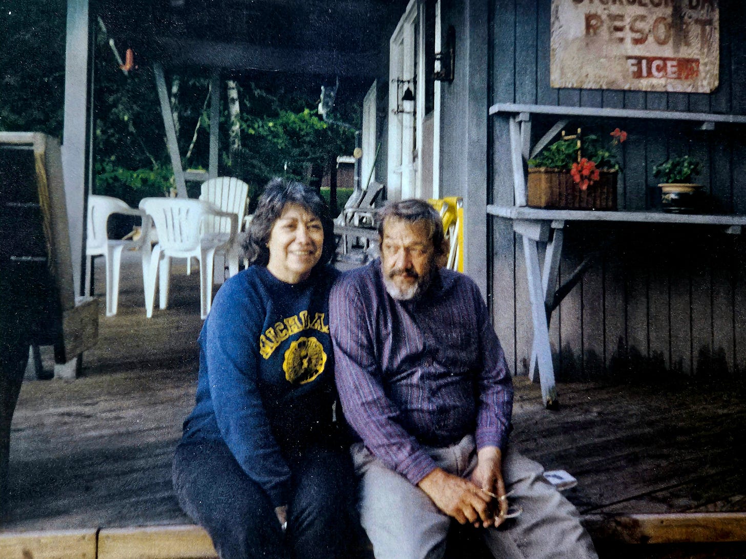 A woman and man sit arm in arm on the steps of a porch