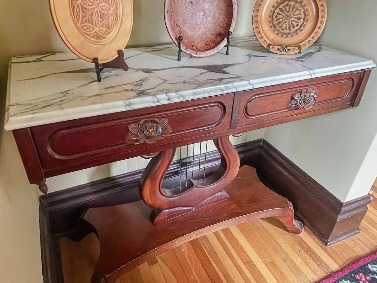 A mahogany entry way table with a white marble top. The draws have carved wooden roses. 