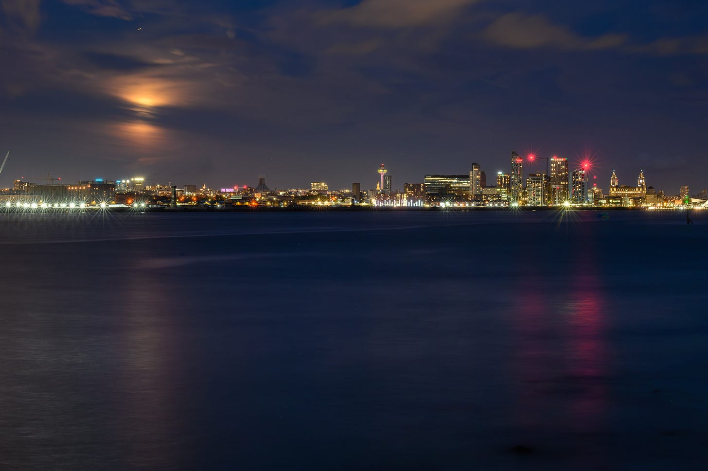 The moon rises behind clouds looking like a spacial anomaly over the city of Liverpool.