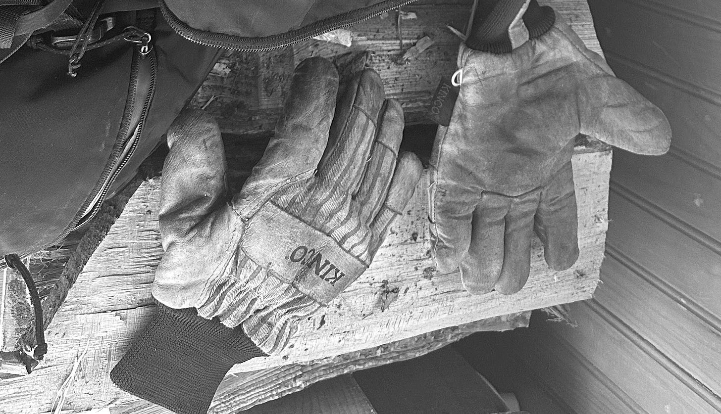 Well-worn pair of leather gloves on stacked wood.