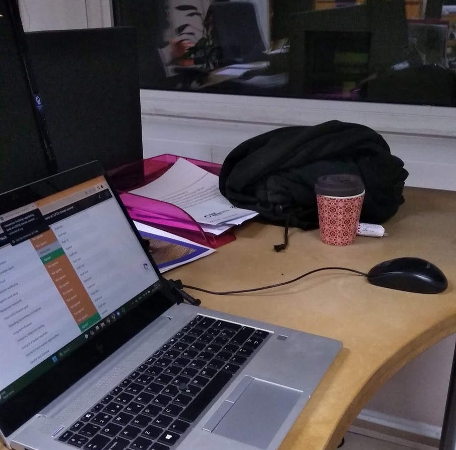 Picture of a laptop in an office after hours with a reusable cup and a mouse beside